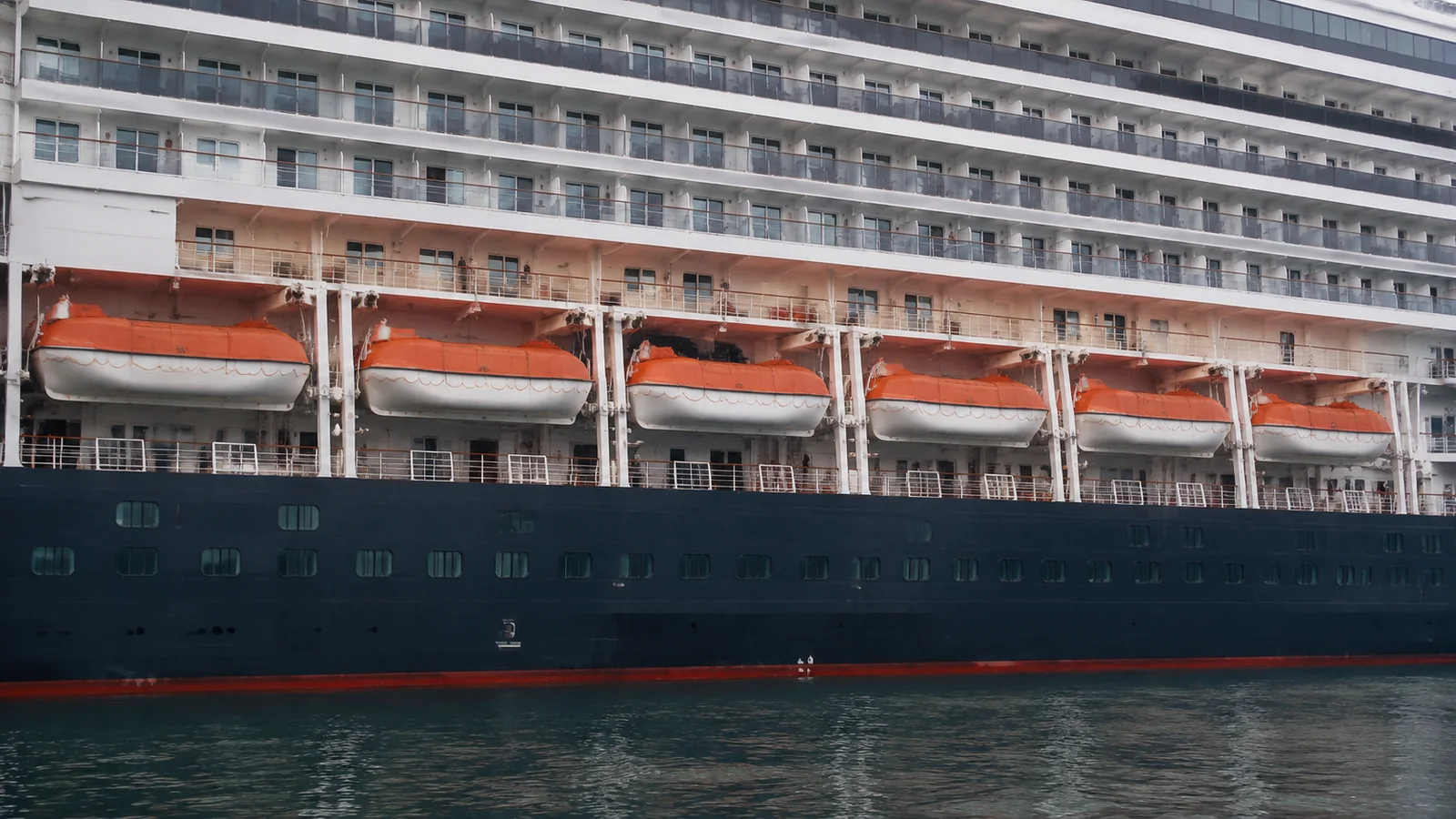 Orange lifeboats line the side of a large cruise ship.