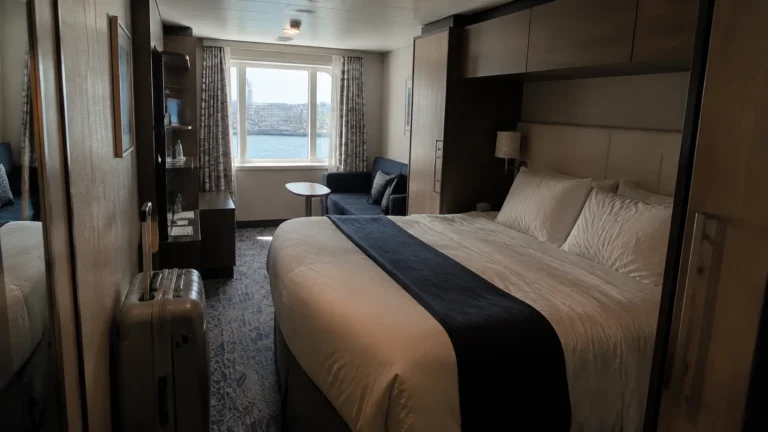 Modern cruise cabin with a double bed and seating area beside a window