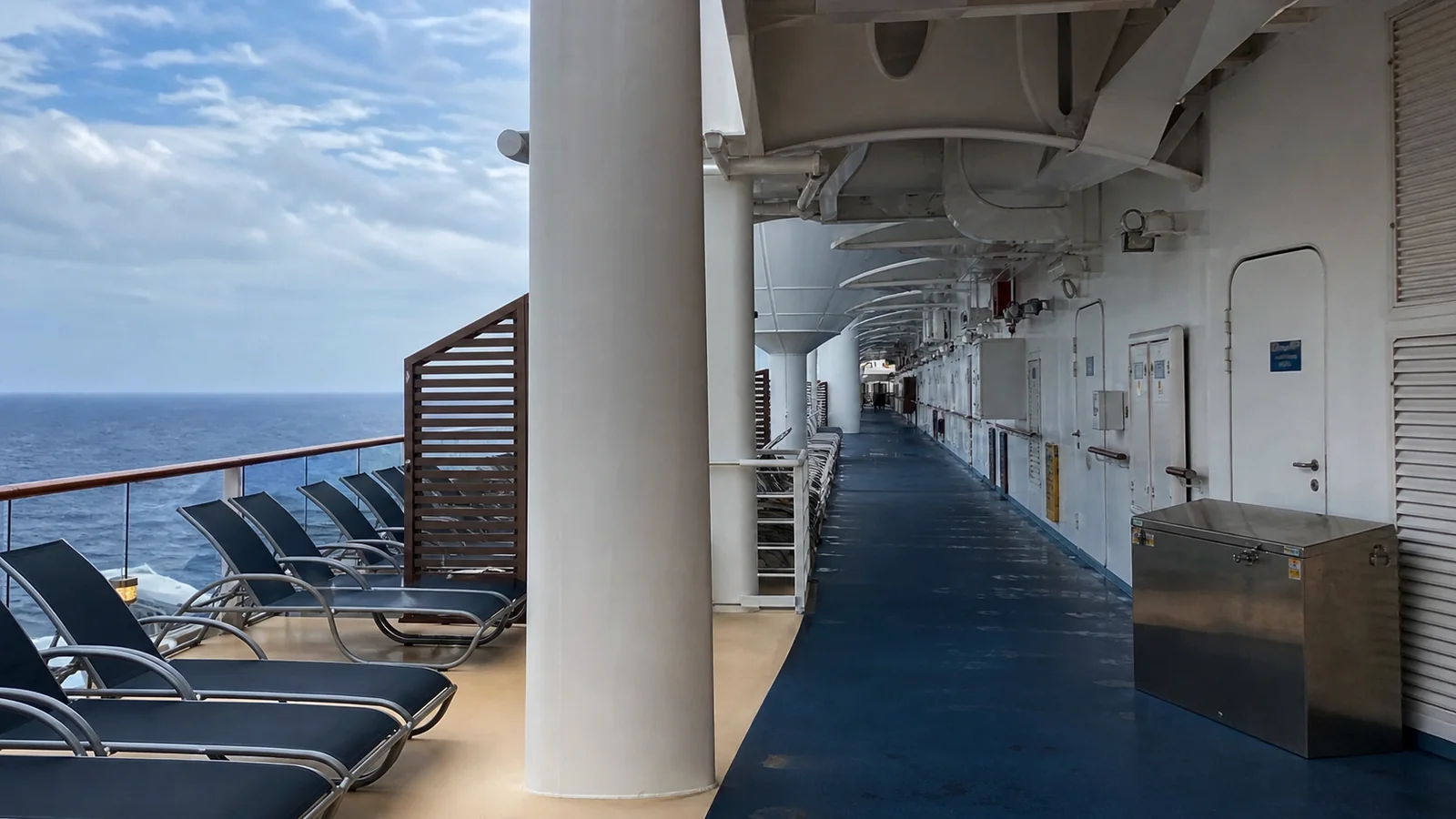Cruise ship promenade with blue flooring and lounge chairs beside the railing