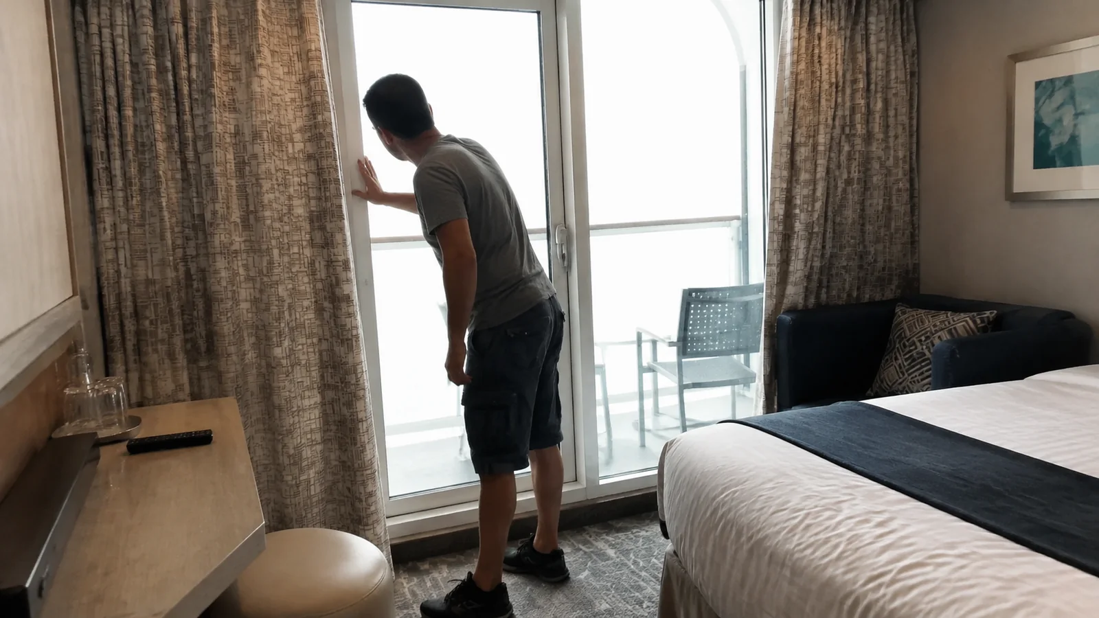 Passenger examining the balcony doorway from inside a cabin.