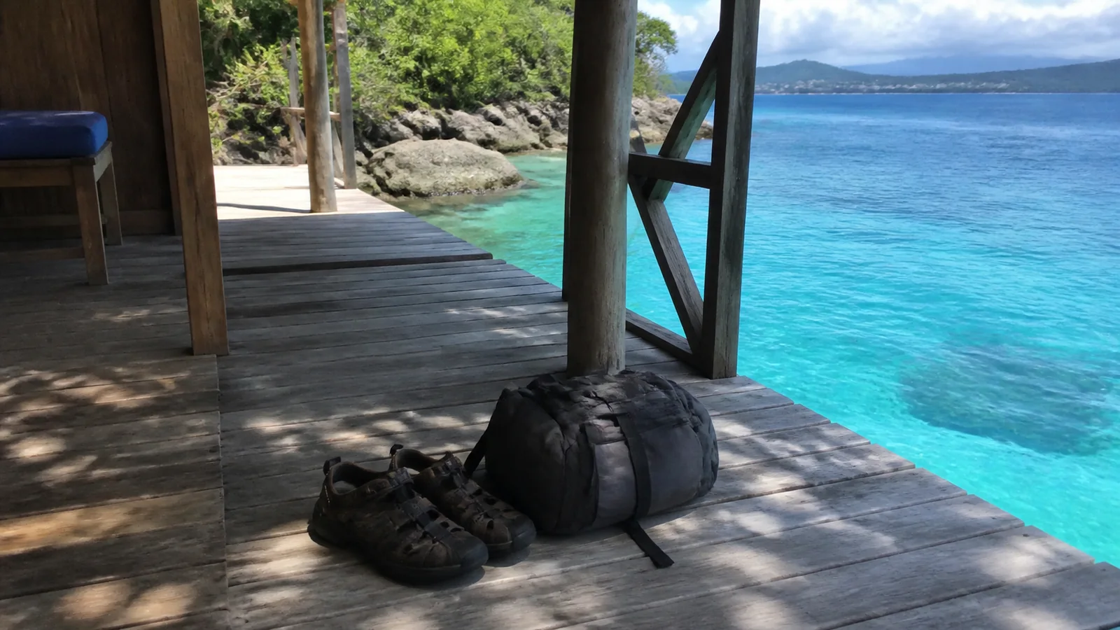 Shoes and a dark duffel bag on a deck beside turquoise water.