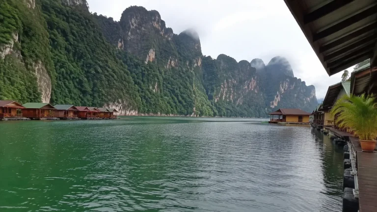 Floating wooden bungalows below towering green limestone cliffs.