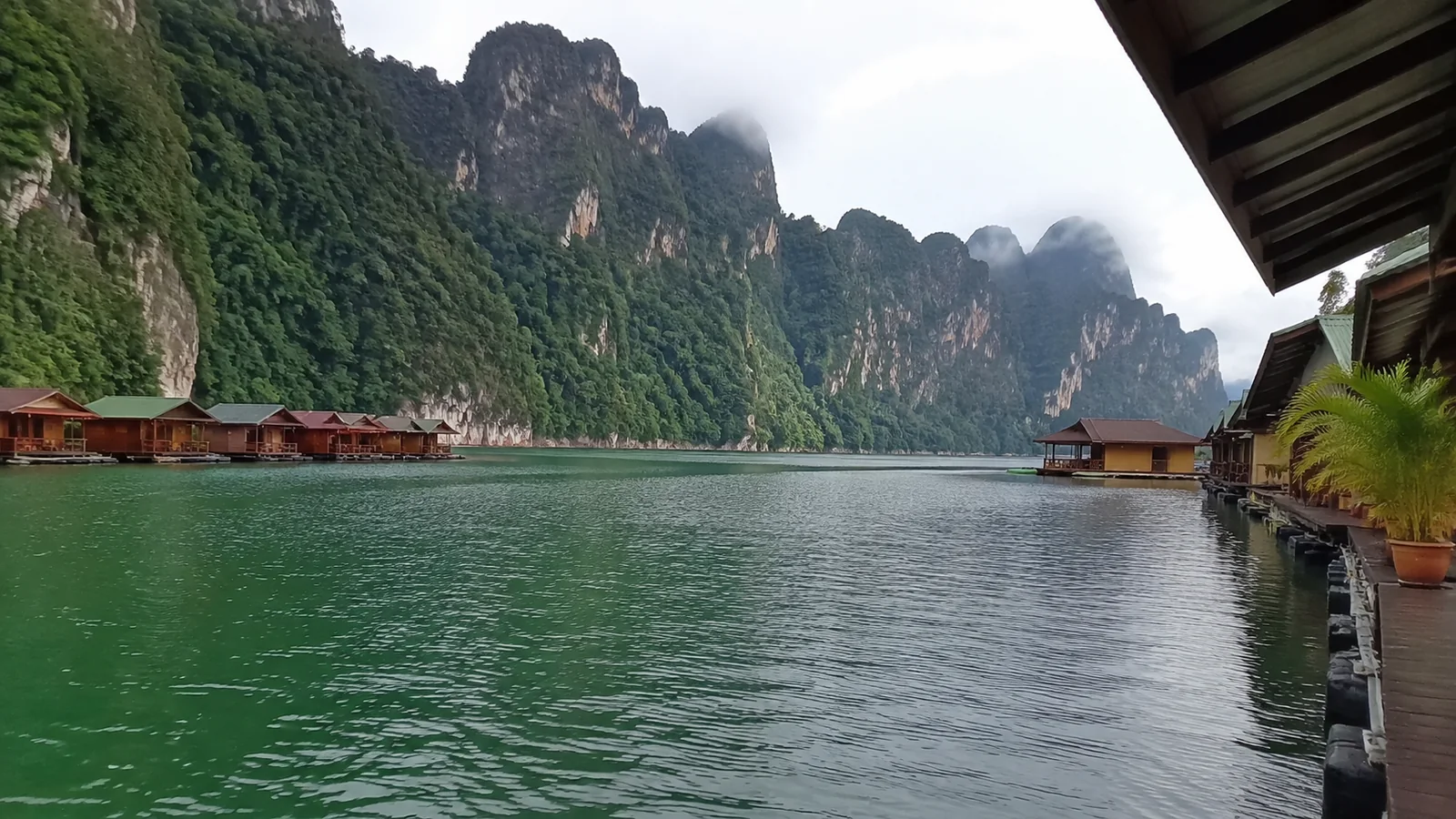 Floating wooden bungalows below towering green limestone cliffs.