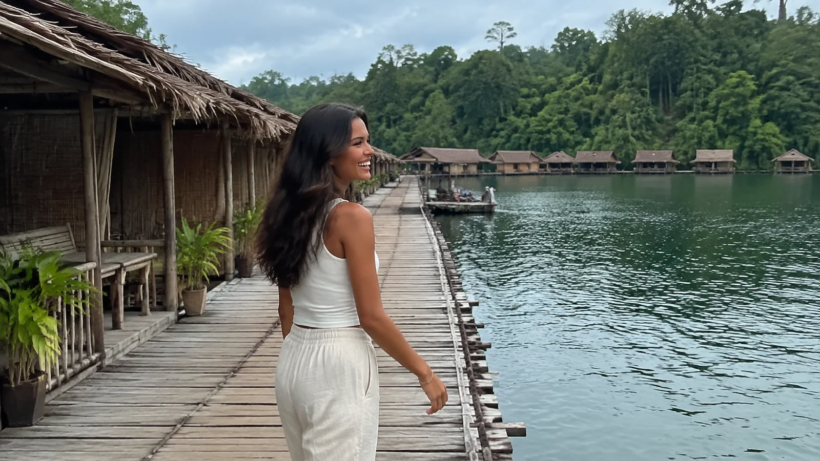 Woman walking a floating boardwalk beside thatched lakeside cabins.