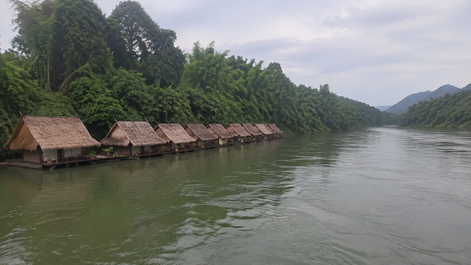 Row of floating thatched bungalows beside a forest-lined river.