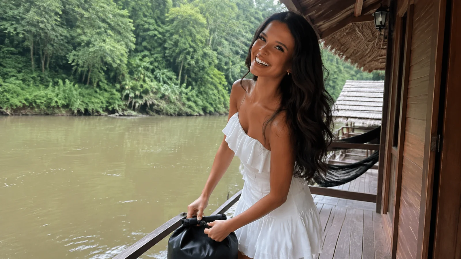 Woman standing on a wooden bungalow porch above a river.