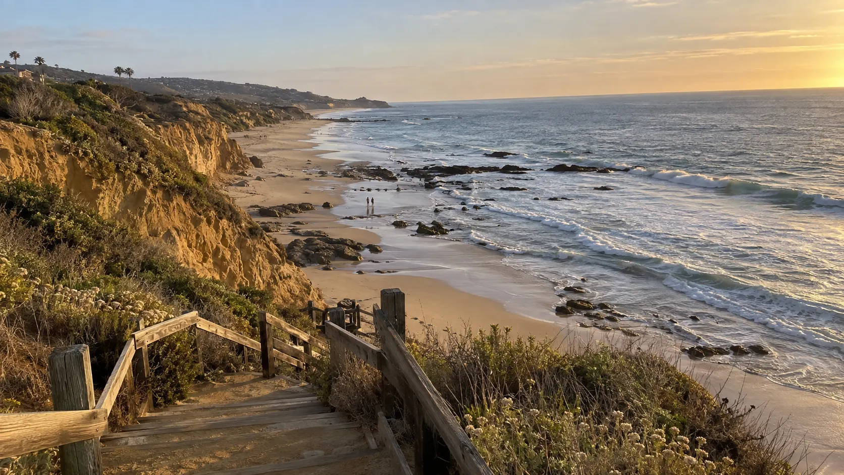 Wooden bluff stairs descending toward a broad Orange County beach at sunset.