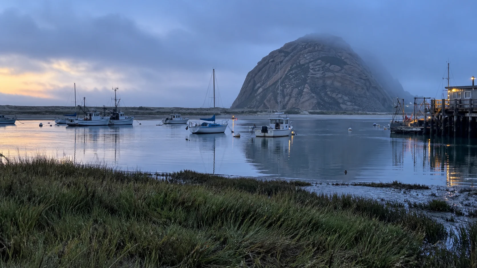 Fishing boats in Morro Bay harbor beneath Morro Rock and low coastal fog.