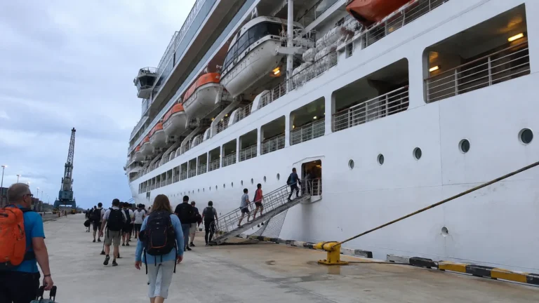 Passengers boarding a docked cruise ship by a side gangway.
