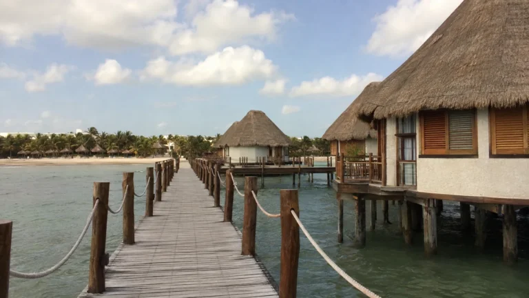 Rope-lined boardwalk leading between thatched overwater bungalows.