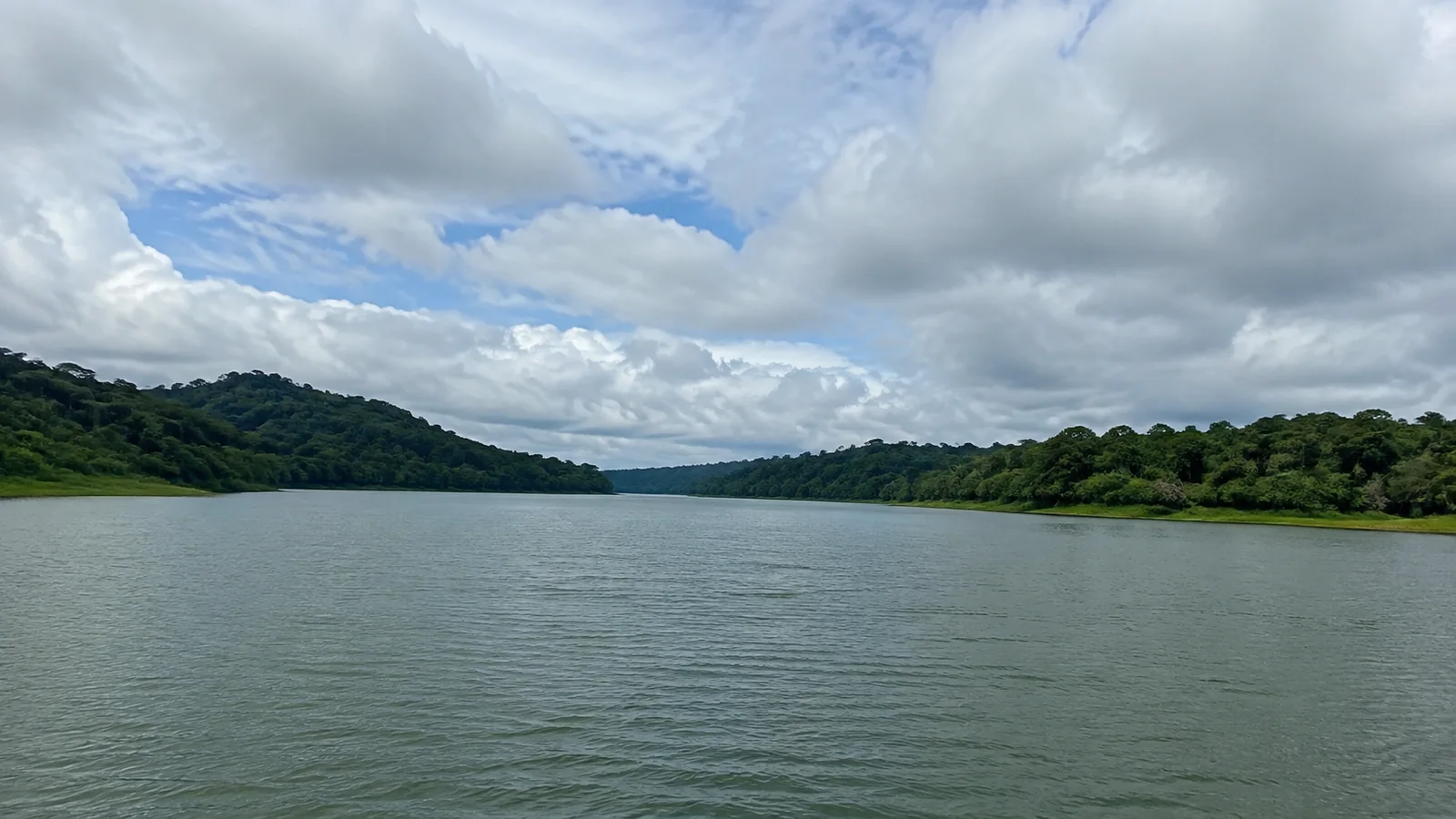 Broad calm channel bordered by dense tropical forest and low hills.