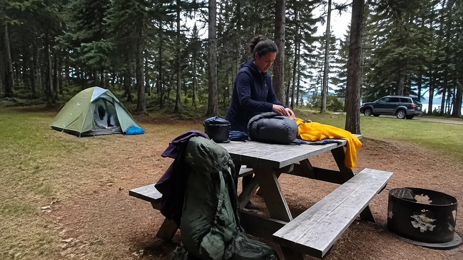 Camper sorting gear on a picnic table beside a forest tent.