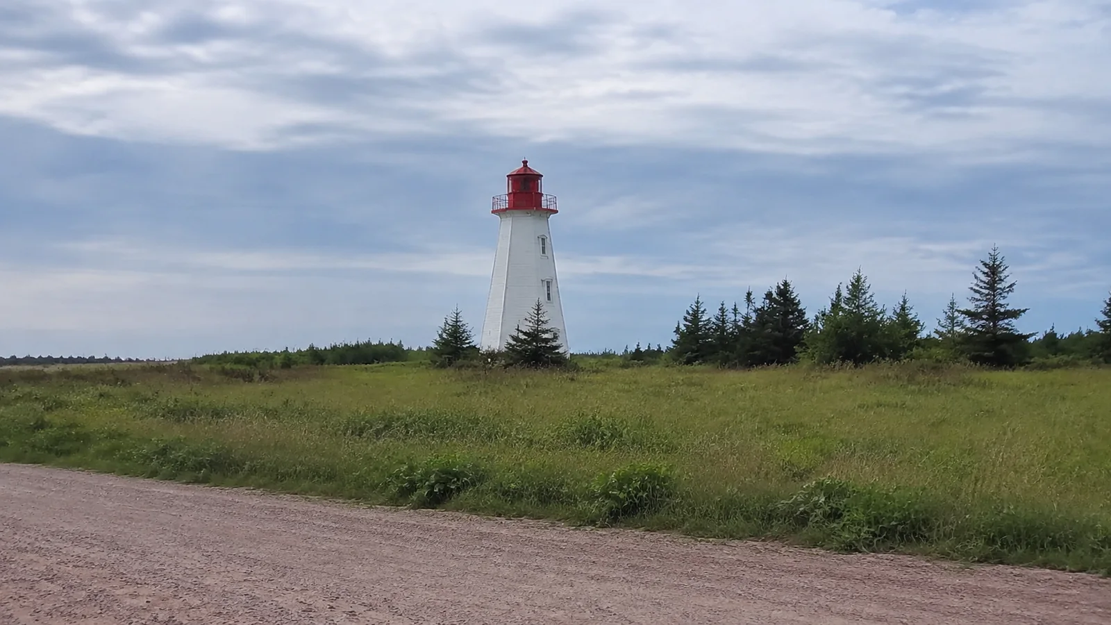 White lighthouse with a red lantern above a grassy coastal field.