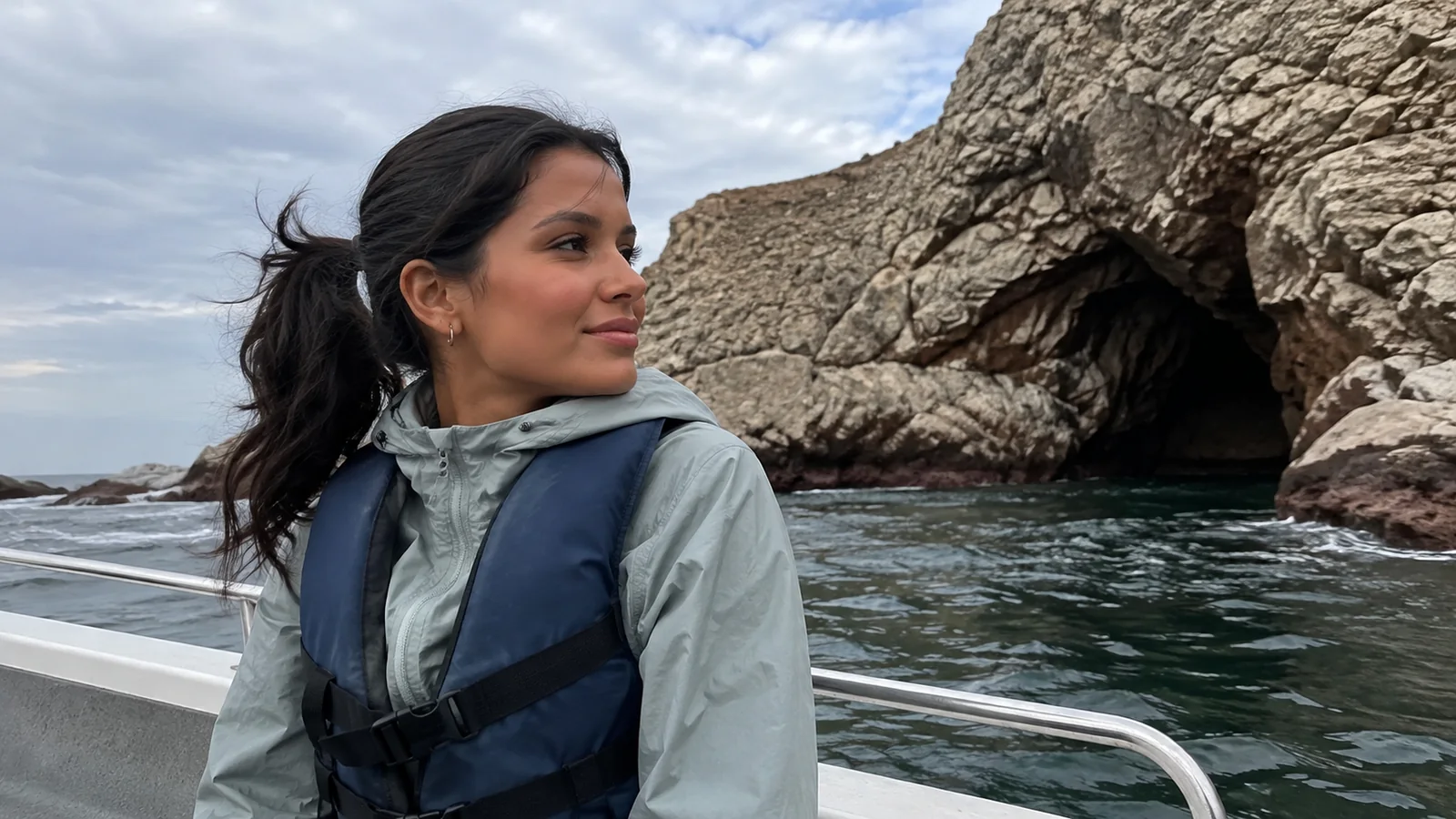 Woman wearing a life jacket aboard a boat near a rocky sea cave.
