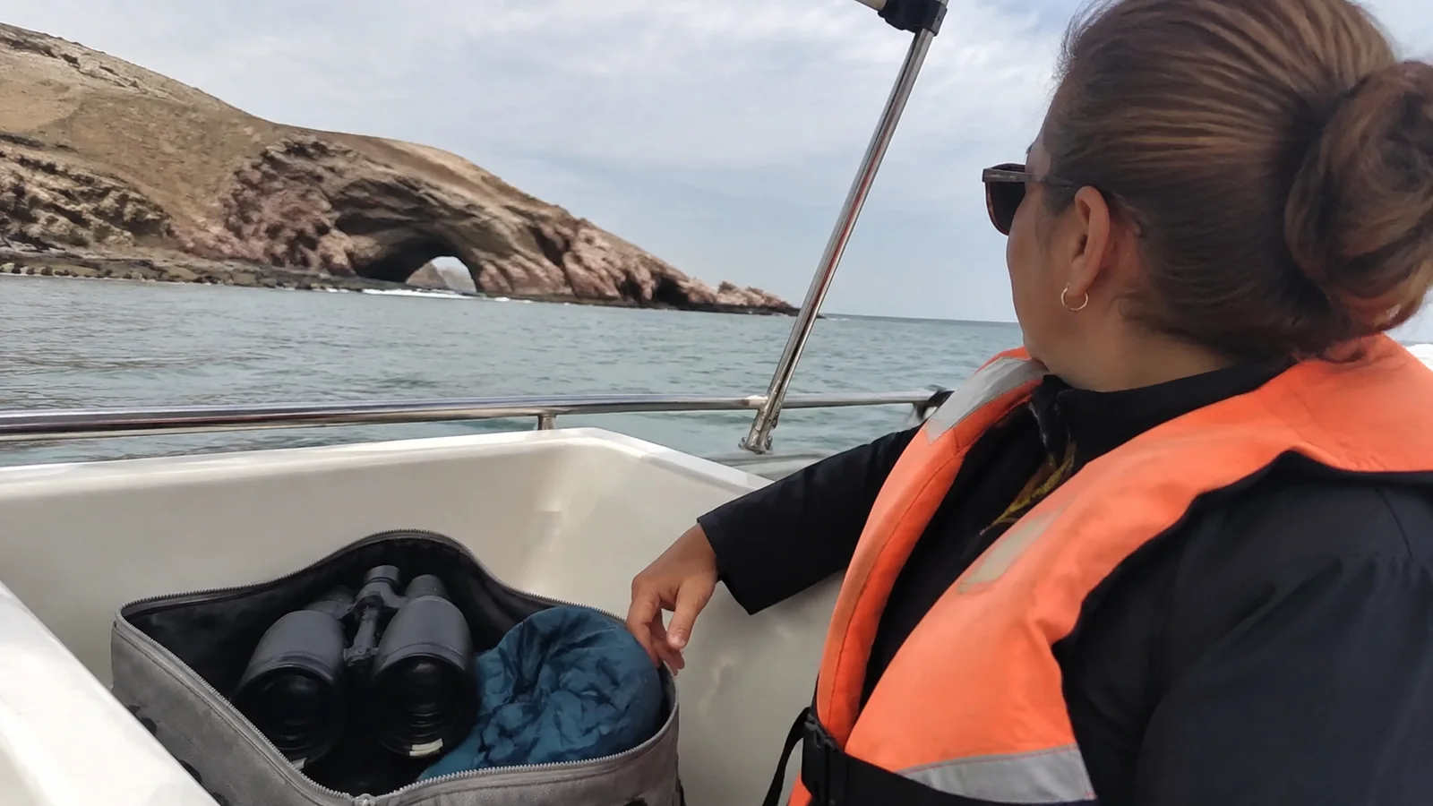Passenger with binoculars and a bag on a coastal boat excursion.