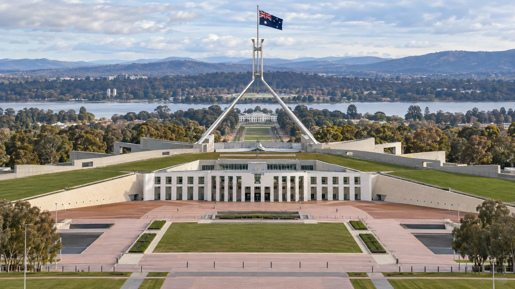 Canberra's Parliament House, grass-covered roof, and flag mast align above Lake Burley Griffin.