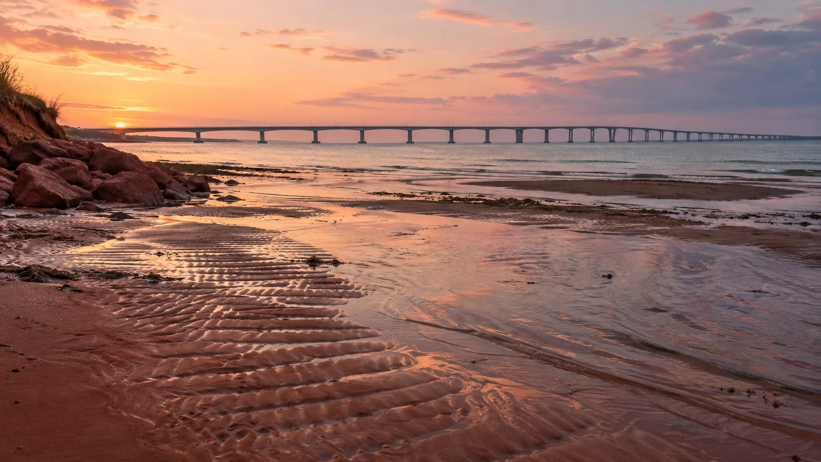 Confederation Bridge spans the horizon beyond Chelton Beach's red tidal sand.