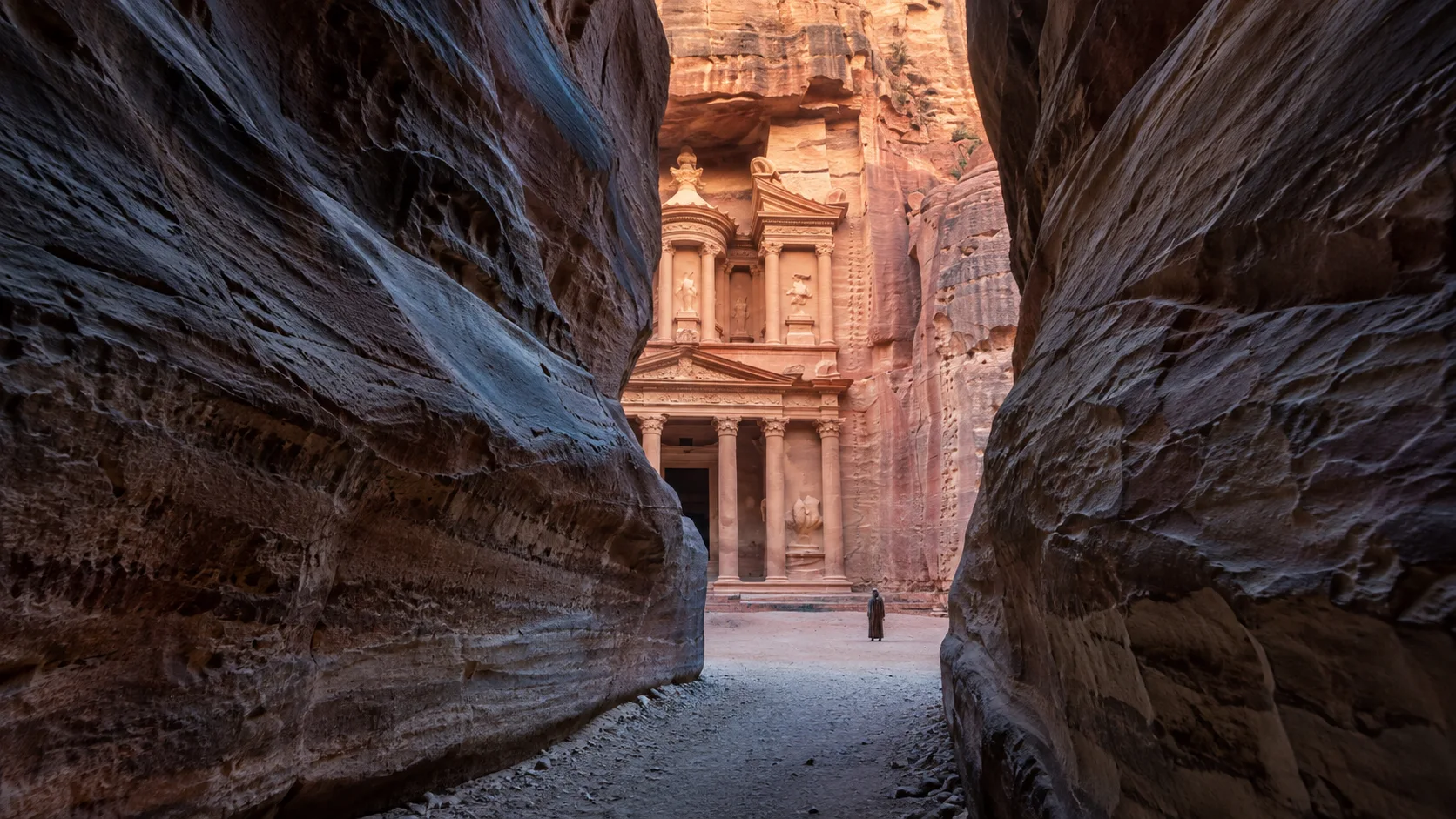 Petra's rose-red Treasury revealed through the shadowed walls of the Siq in early morning.