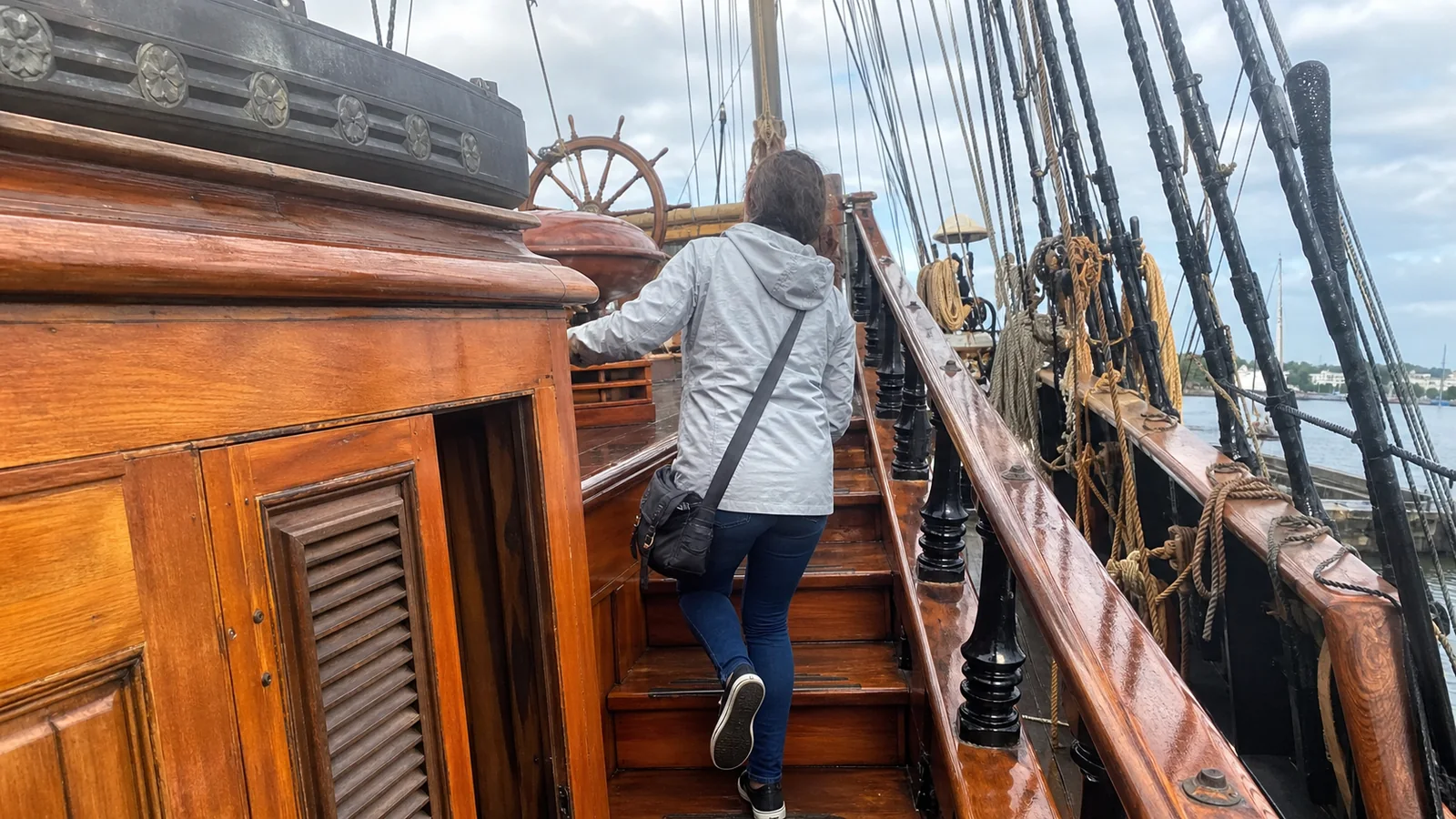 Visitor climbing wooden stairs to the upper deck of a sailing ship.
