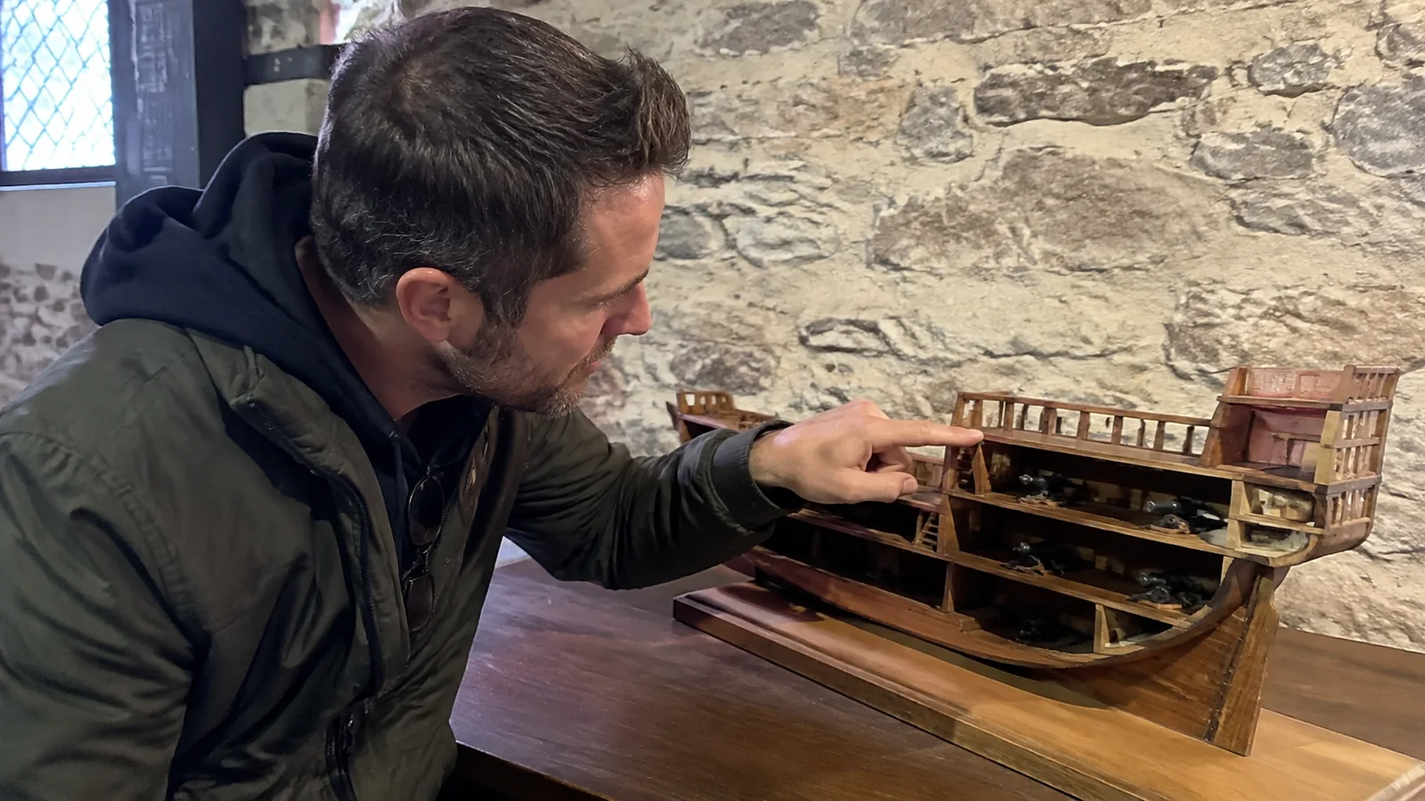Visitor examining the stern section of a wooden ship model.