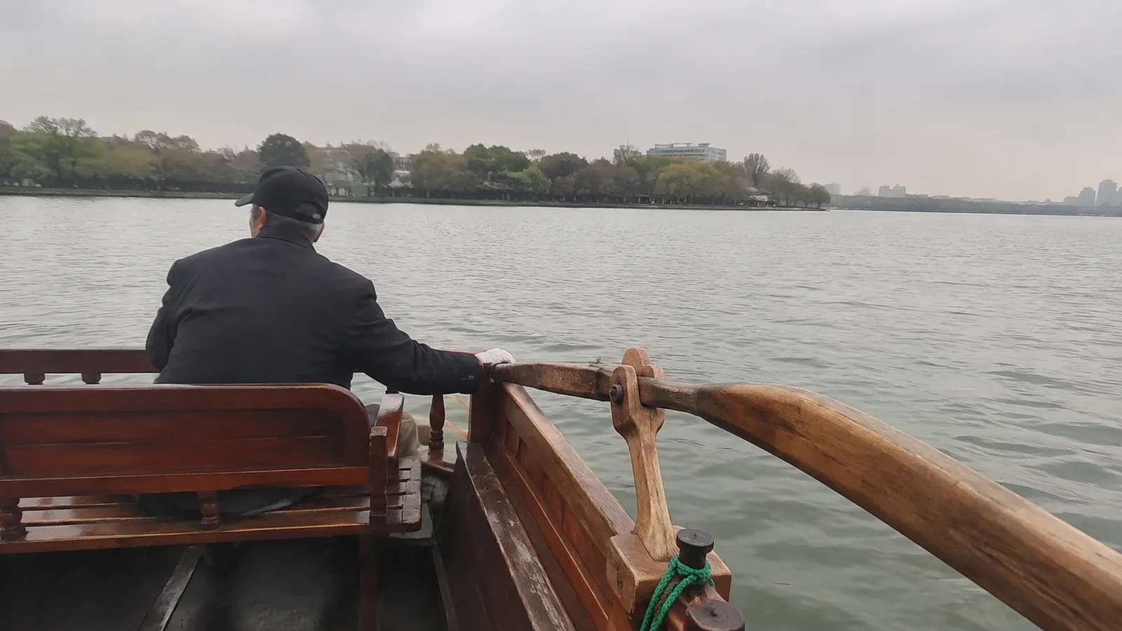 Passenger seated beside a wooden boat railing facing the shoreline.