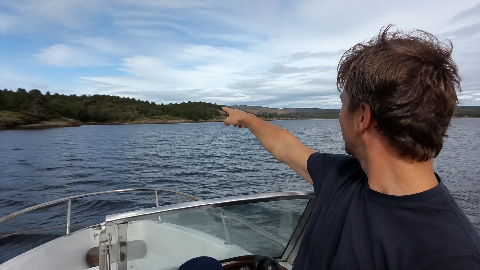 Passenger pointing toward land from the bow of a small boat.