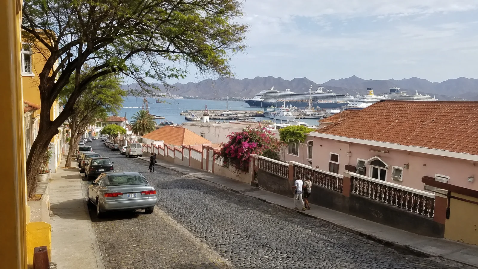 Cobblestone street descending toward a harbor with cruise ships and mountains