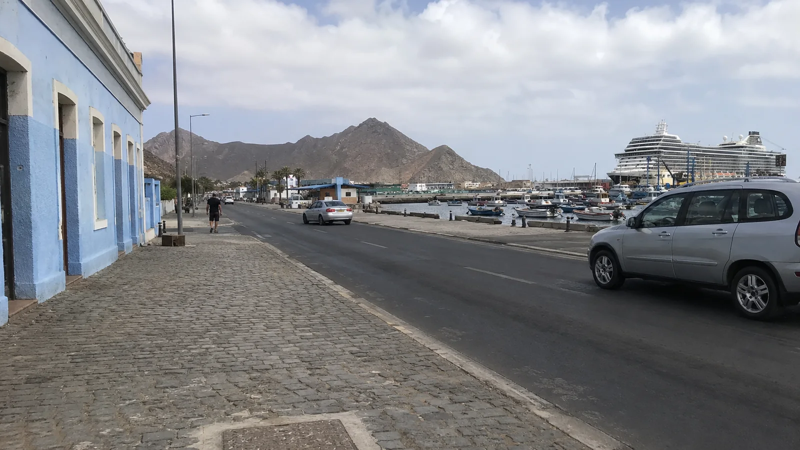 Waterfront street with cruise ships docked below rugged mountains