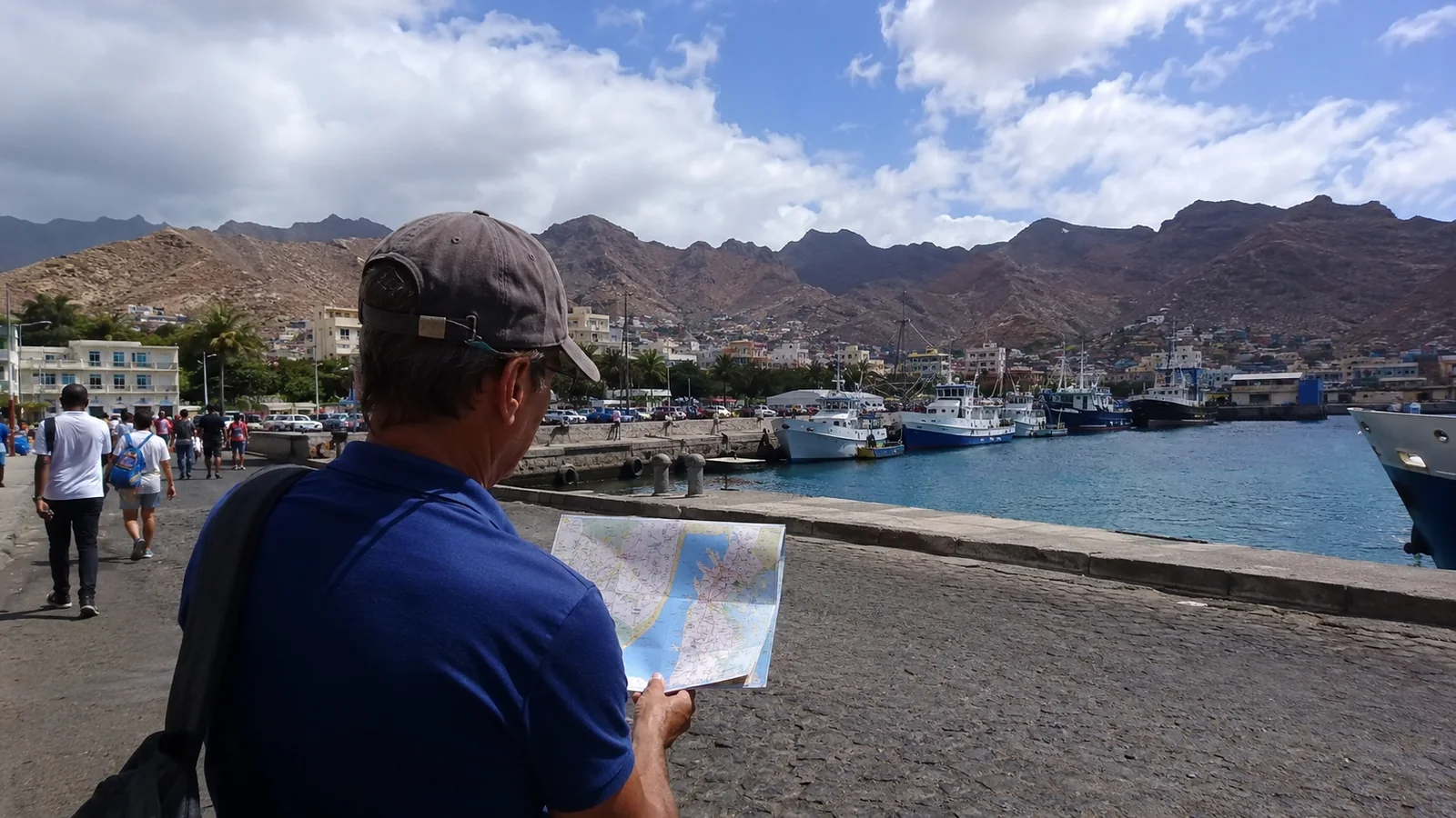 Man holding a map at a waterfront overlooking a mountain harbor