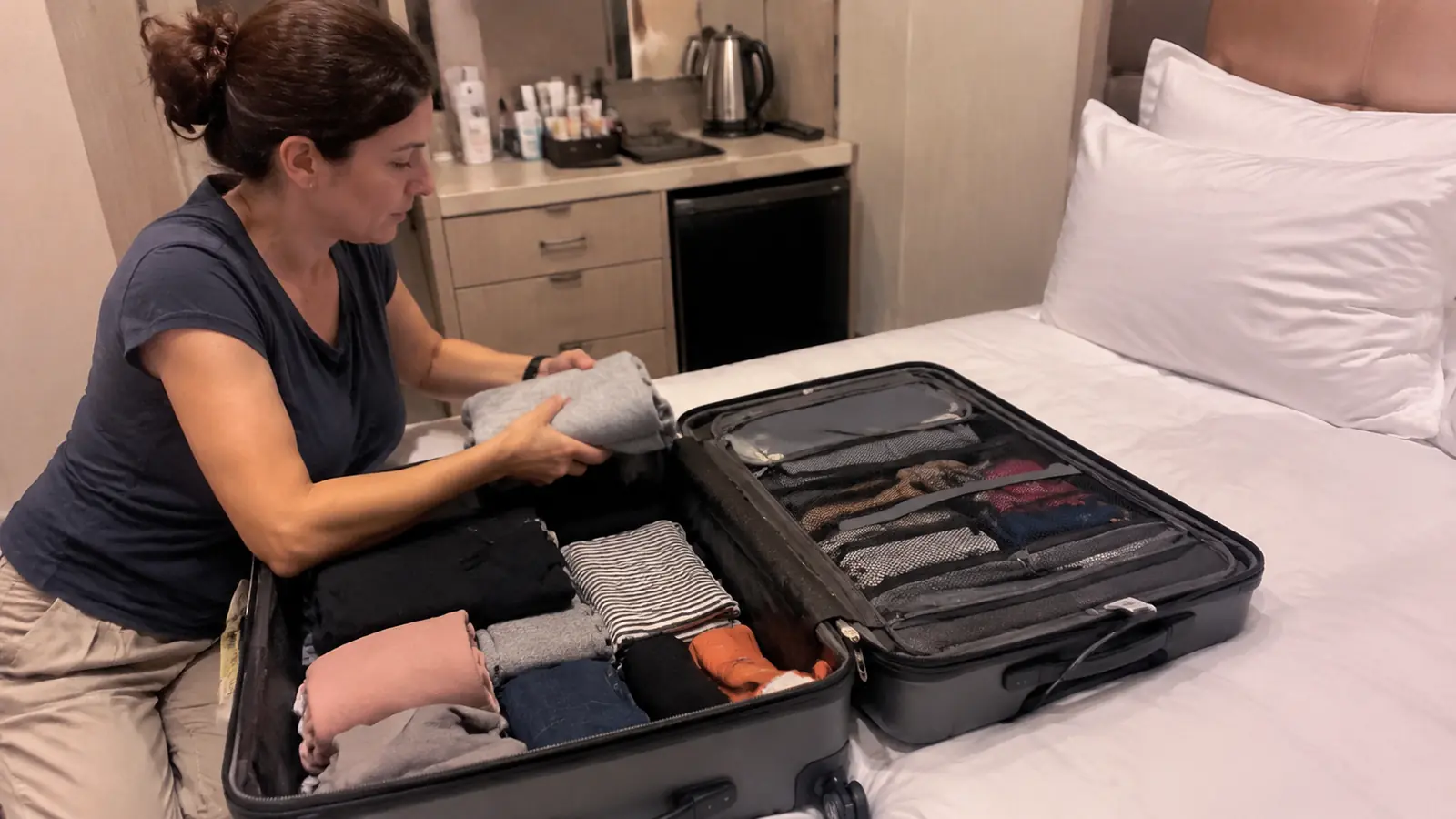 Woman packing folded clothes into an open suitcase on a cruise cabin bed
