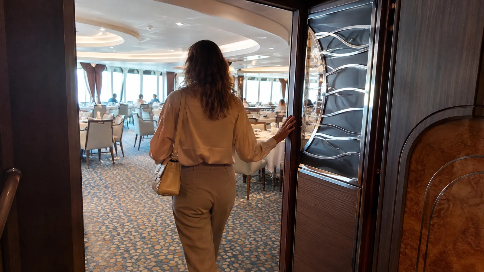 Passenger in a blouse and trousers entering an elegant ship dining room.