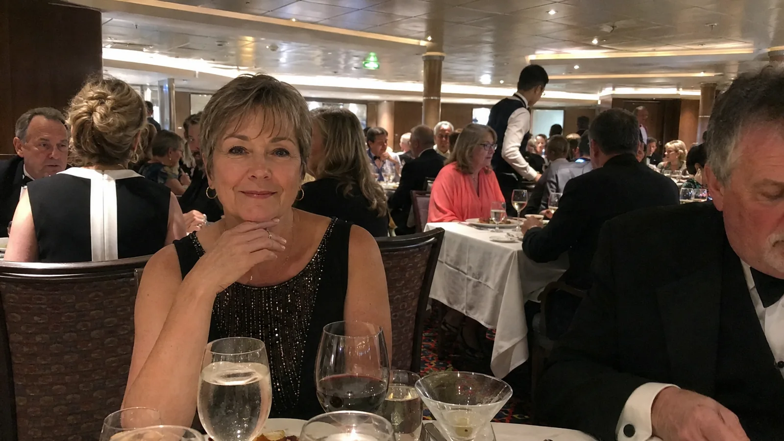 Passengers dressed for dinner at white-clothed dining tables.