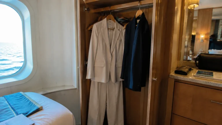 Light-colored suit and dark formal outfits hanging in a cabin wardrobe.