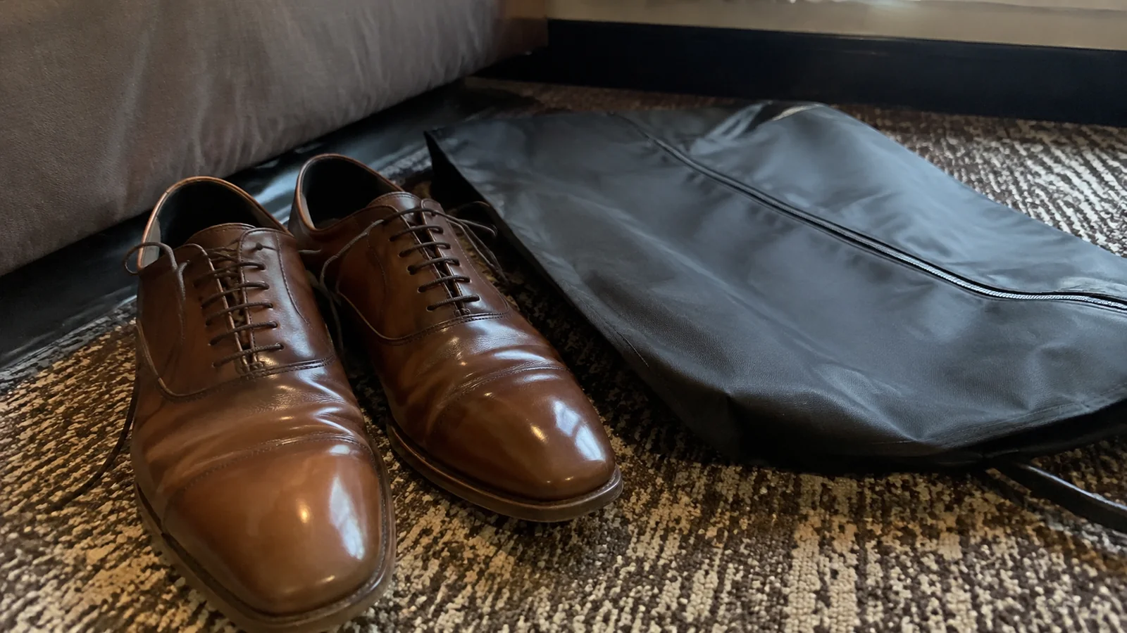 Polished brown shoes beside a zippered garment bag.