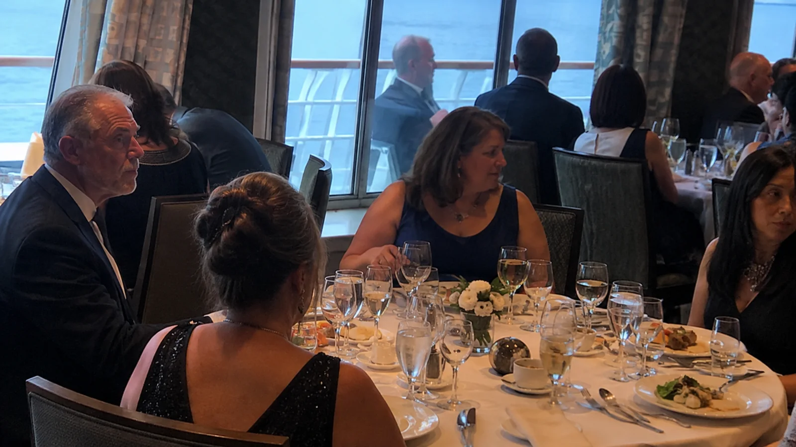 Passengers dressed for a formal dinner around a shipboard table.