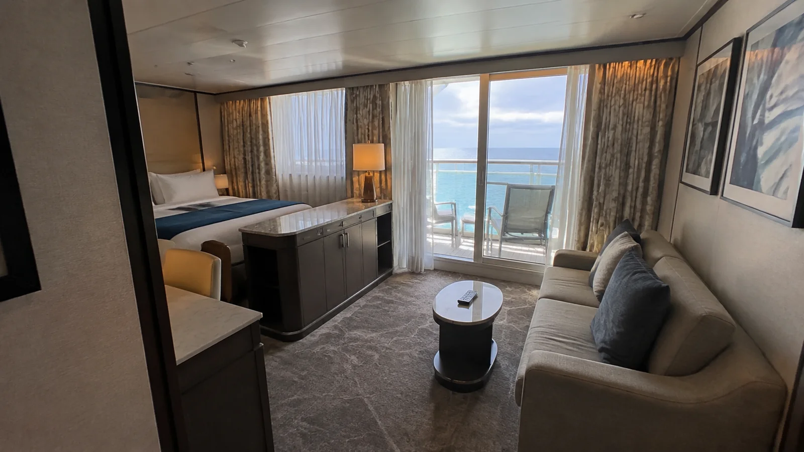 Stateroom sitting area contains a sofa, round table and balcony doors.