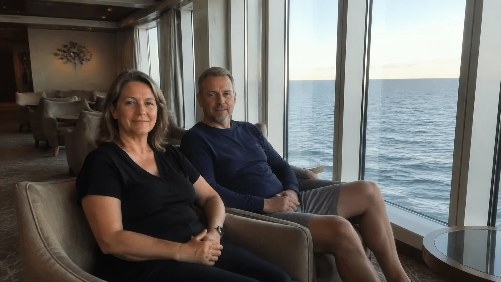 Couple sits in armchairs beside large windows overlooking the sea.