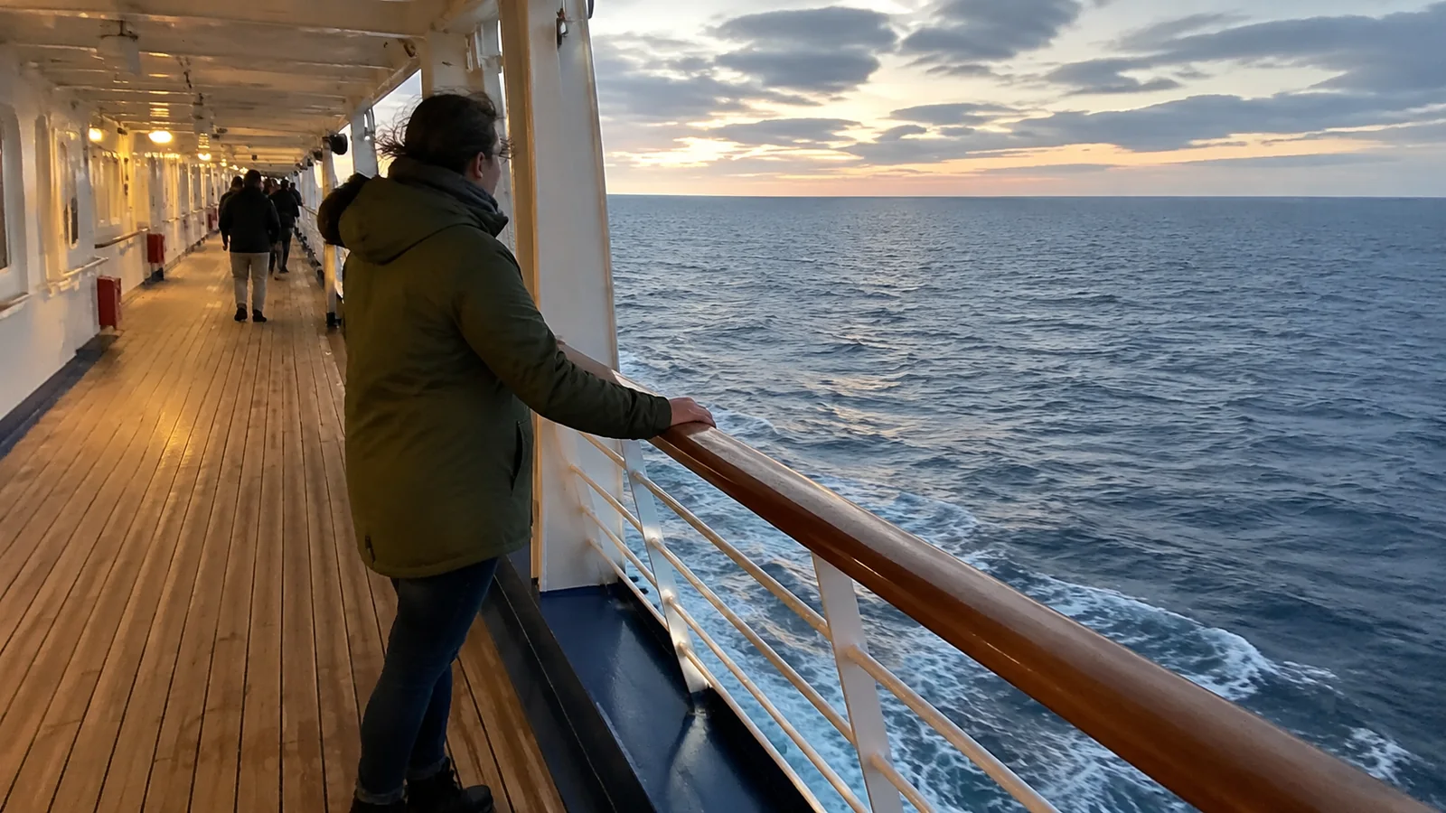 Passenger standing at a cruise ship promenade railing at sunset
