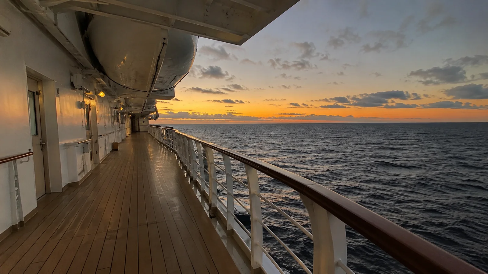 Empty cruise ship promenade deck with lifeboats overhead at sunset