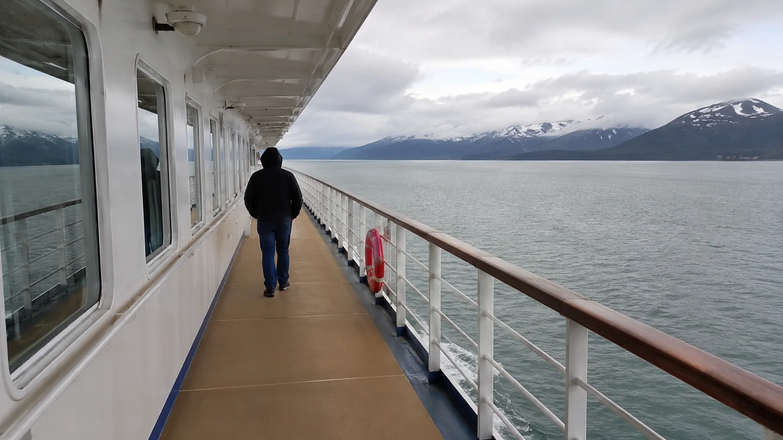 Person walking along a cruise ship promenade deck overlooking mountains and water