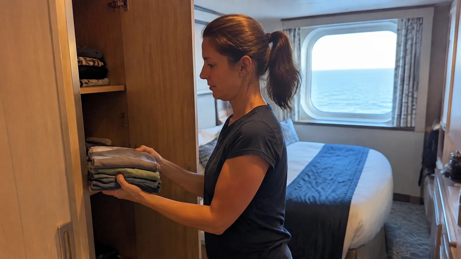 Passenger placing folded clothing on a cabin wardrobe shelf.