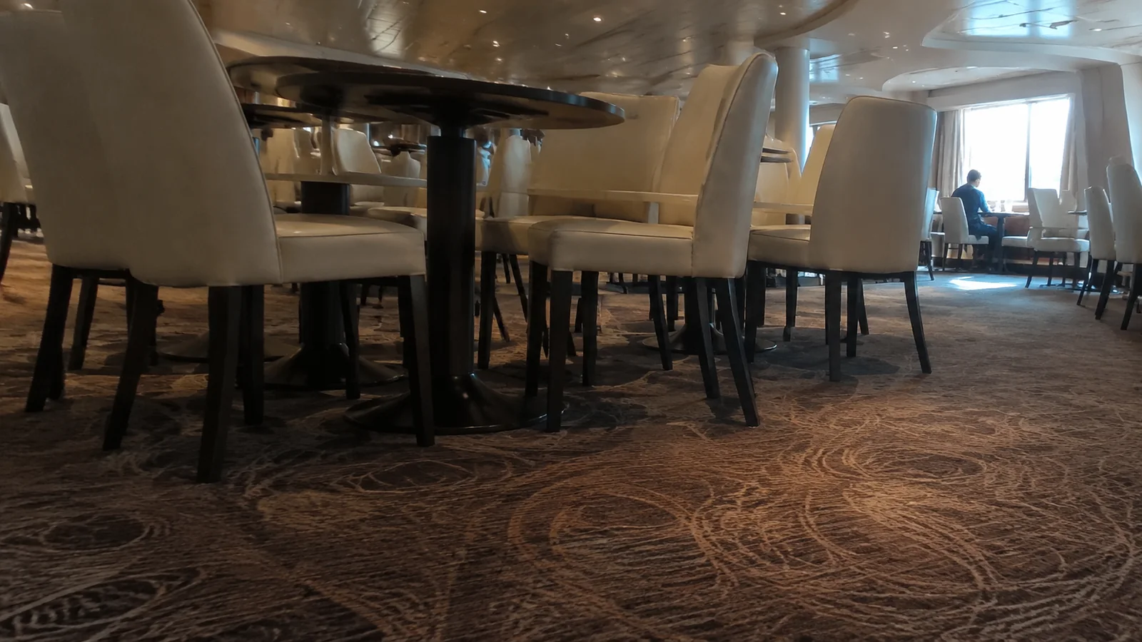Dining chairs and tables on a carpeted ship restaurant floor.