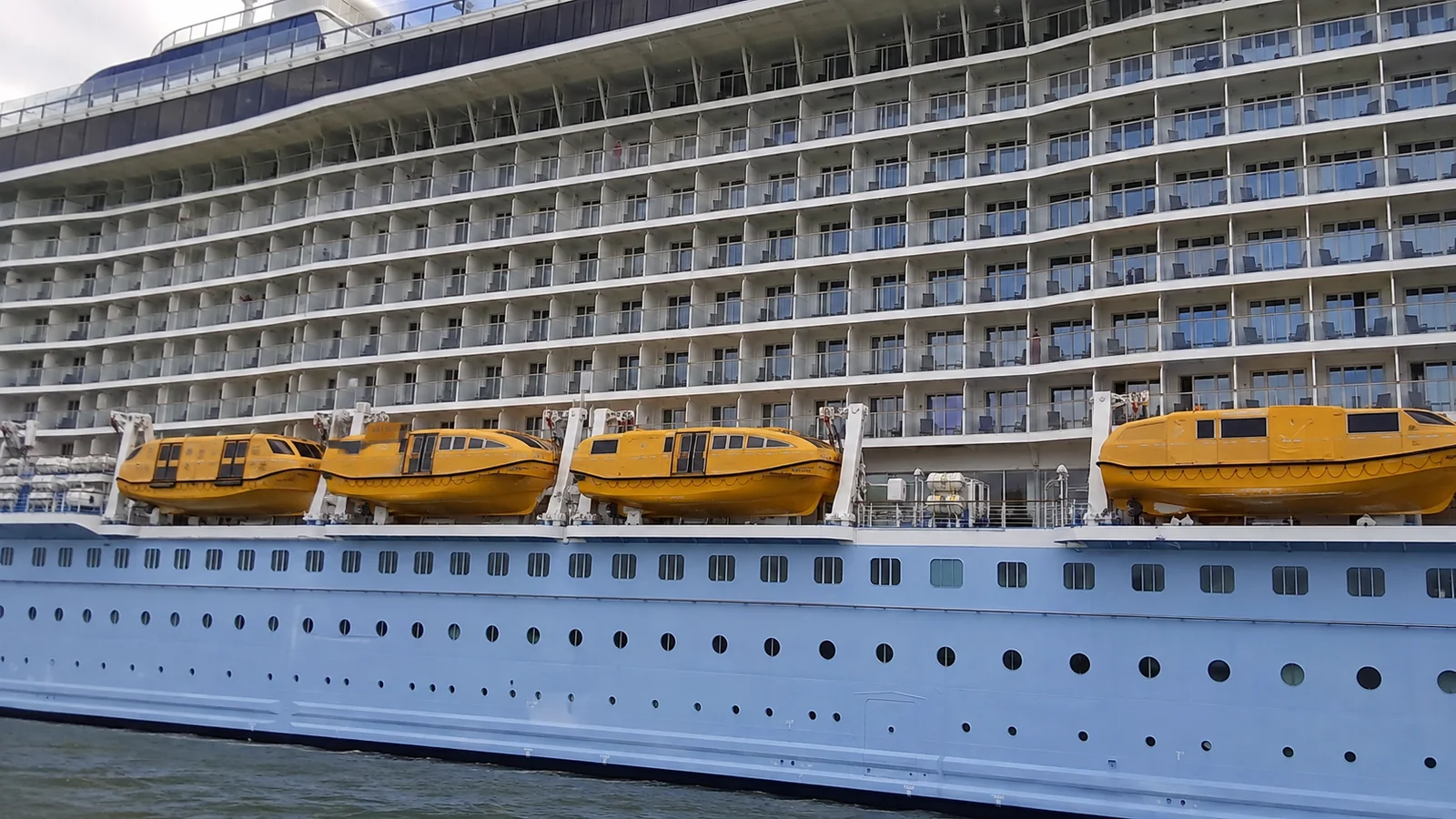 Rows of balconies above yellow lifeboats on a cruise ship's side.