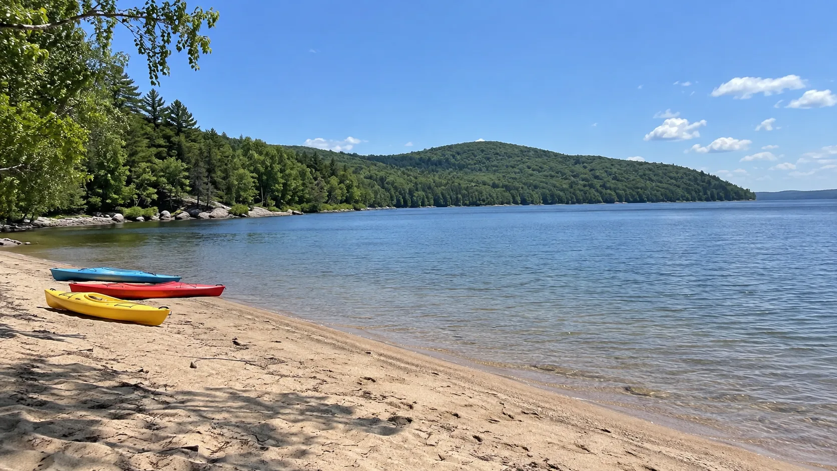 Colorful kayaks resting on a sandy lake beach in a water-centered Quebec park.