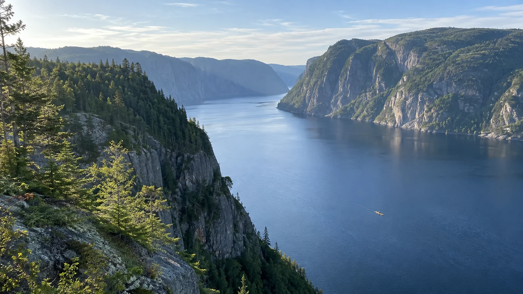 Forested cliffs plunging into the deep blue water of Saguenay Fjord.