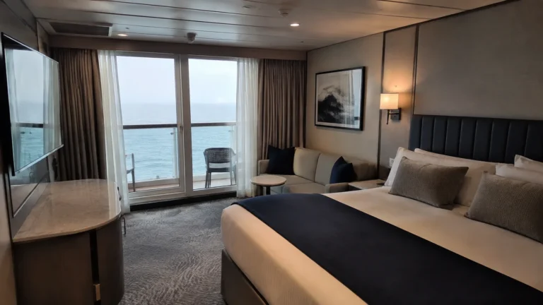 Cruise stateroom with a double bed, sofa and glass doors opening onto an ocean balcony.