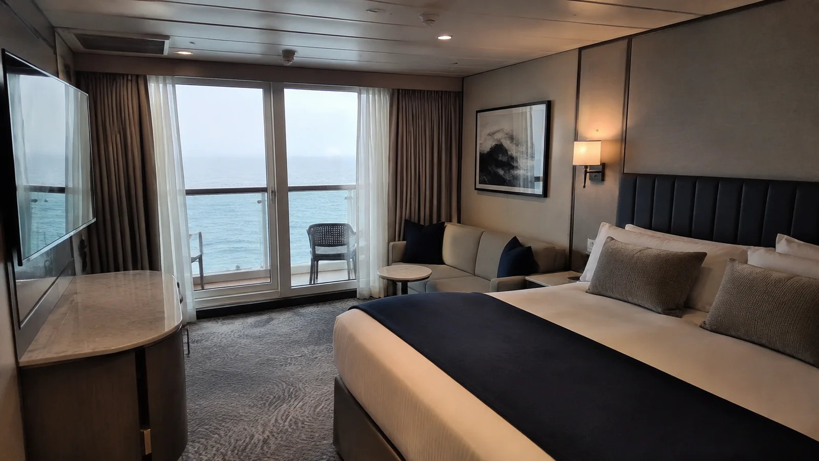 Cruise stateroom with a double bed, sofa and glass doors opening onto an ocean balcony.