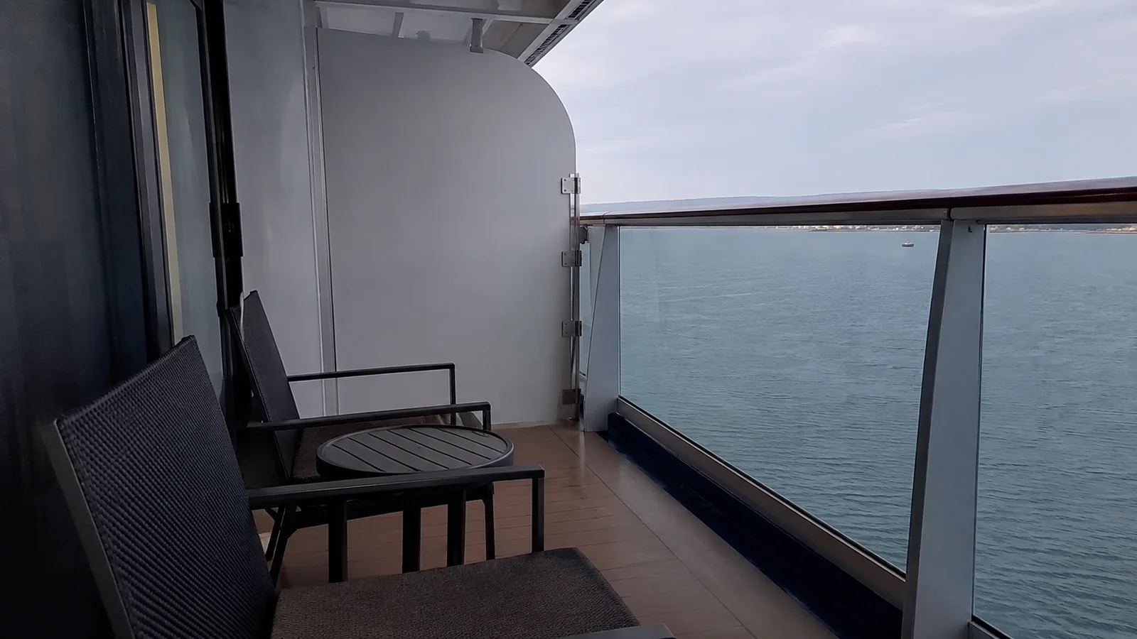 Two chairs and a small table face the ocean on a sheltered balcony.