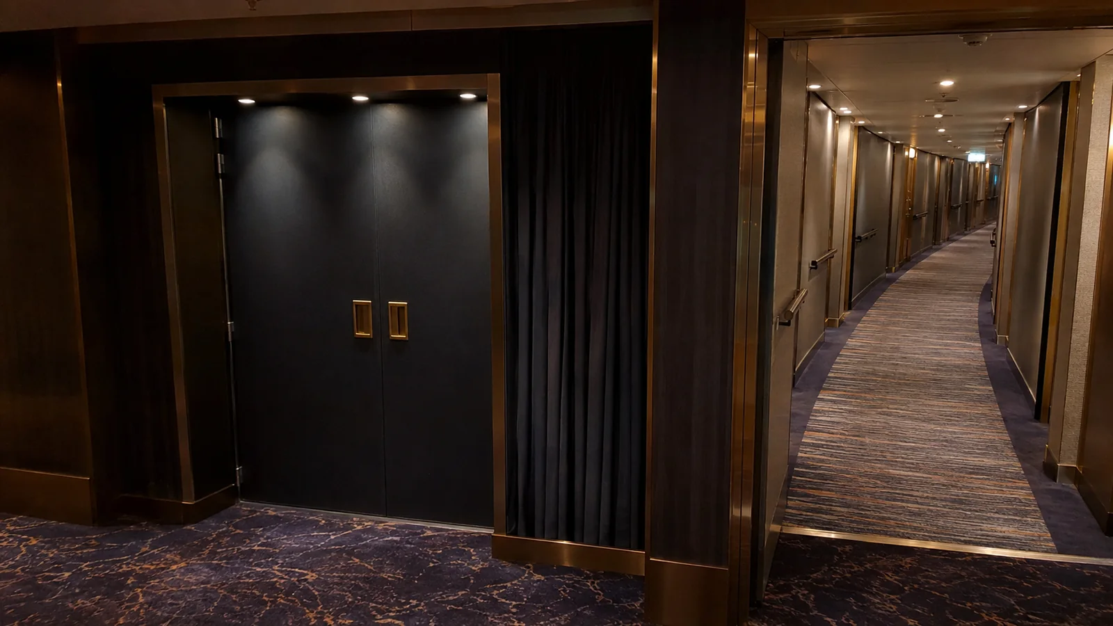 Closed double doors stand beside a long carpeted ship corridor.