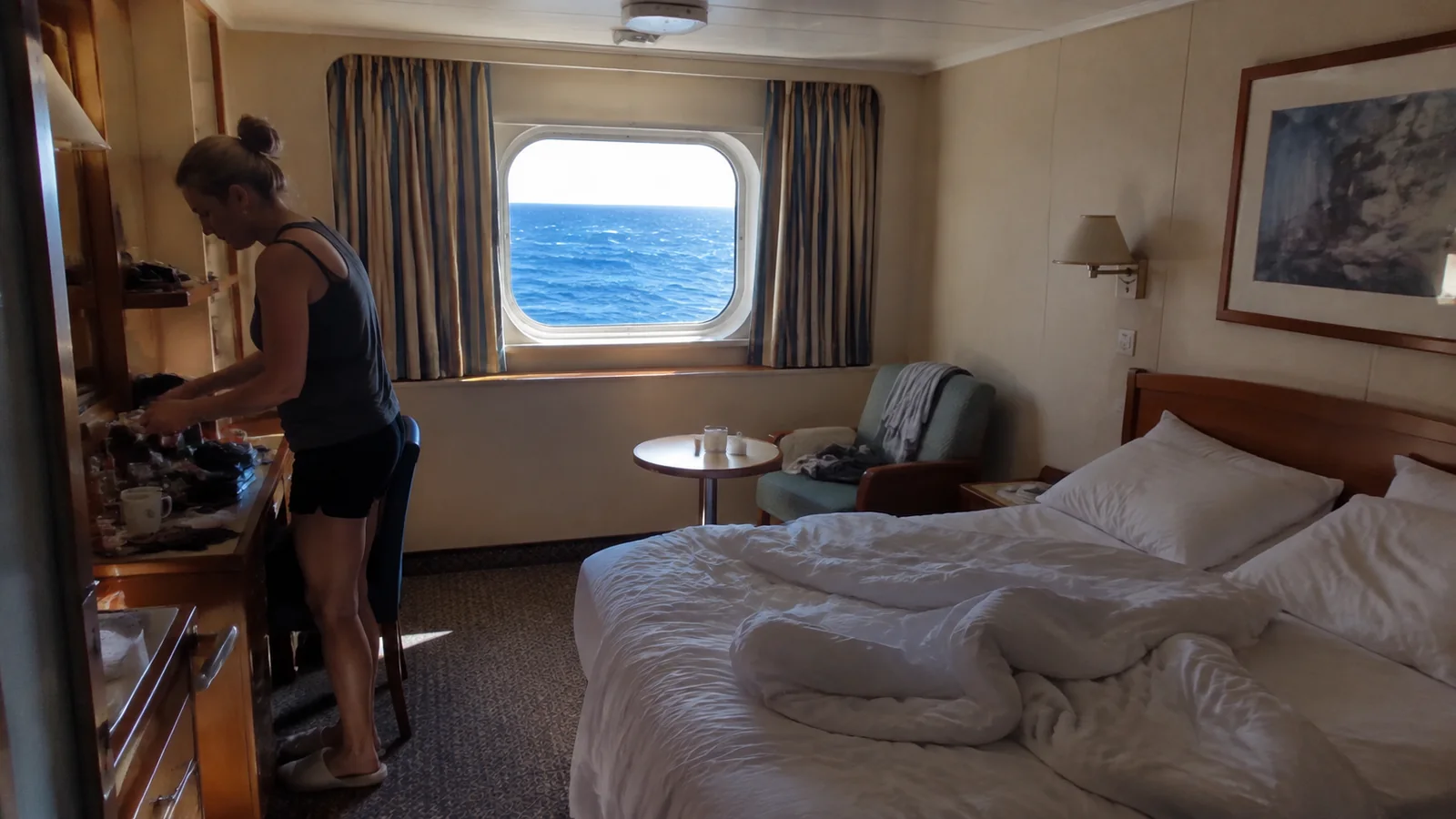 Passenger unpacking at a desk in an ocean-view cabin.